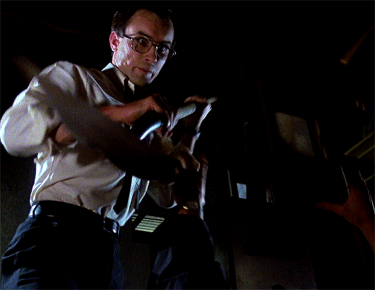 A gif of a man wearing glasses, a white buttoned shirt, a black tie and black pants, stabbing a person offscreen with a shovel. Blood splatters on his clothes as the person's arms flail.
