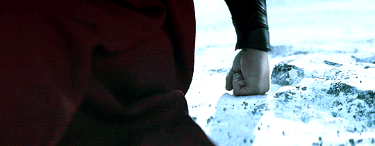 A GIF of Superman getting ready to fly. His fist is rested on the ground as particles of the ground vibrate around it.