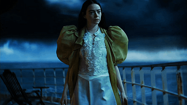 A GIF showing a scene from the movie 'Poor Things'. A white woman with waist length dark hair walks barefoot towards the guard rail on a ship and looks out to sea. She is wearing a short white dress with ruffles on the bodice and a yellow robe with short puffy sleeves.