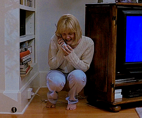 A GIF of a woman crouching next to a TV while crying into a phone.