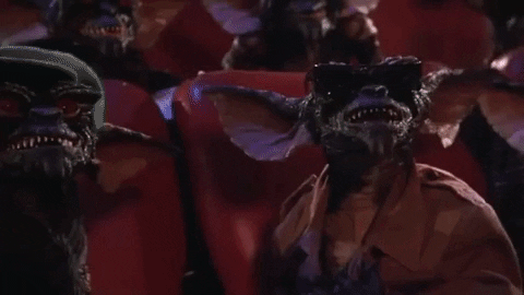 A GIF of gremlins in a movie theatre. They start laughing and throwing popcorn around.
