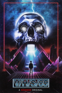 Poster for the movie 'V/H/S/85'. A shadowy person stands underneath a flight of stairs and a giant metallic skull with a beam of light coming from its mouth.