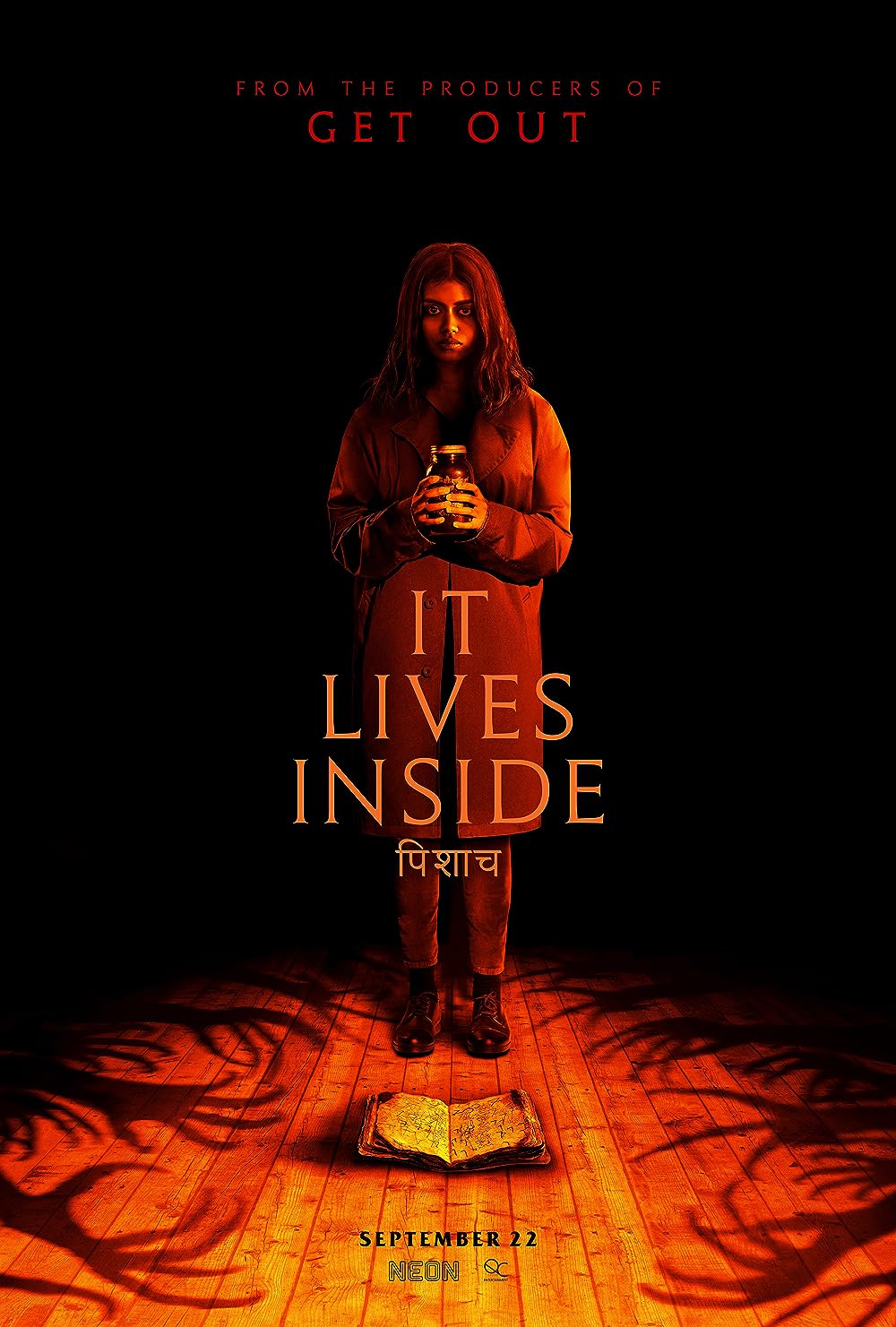 Poster for the film 'It Lives Inside'. A young girl stands against a black background while holding a jar and lit in red. The shadows on the floor around her look like hands. The title of the film is laid over her in capitals with Indian script underneath (I don't know which one I'm very sorry)