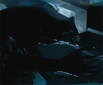 A gif of a large black alien with an elongated head moving slowly