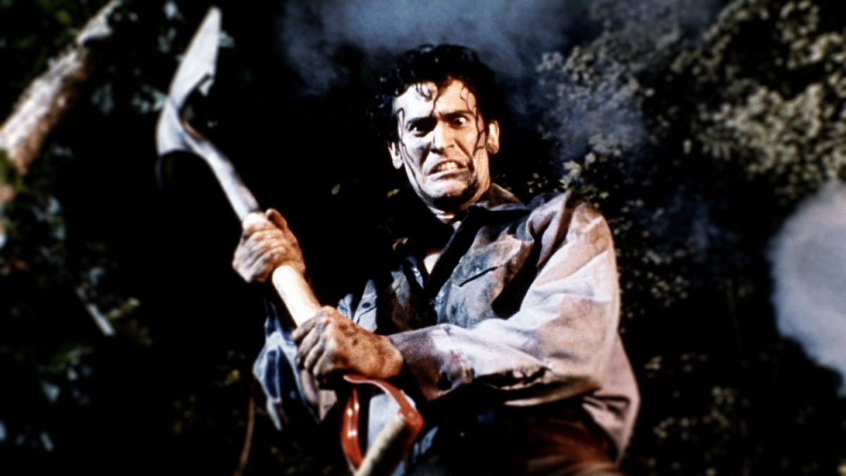 A still from 'Evil Dead II'. A young man with blood running down his face looks scared while holding an axe.