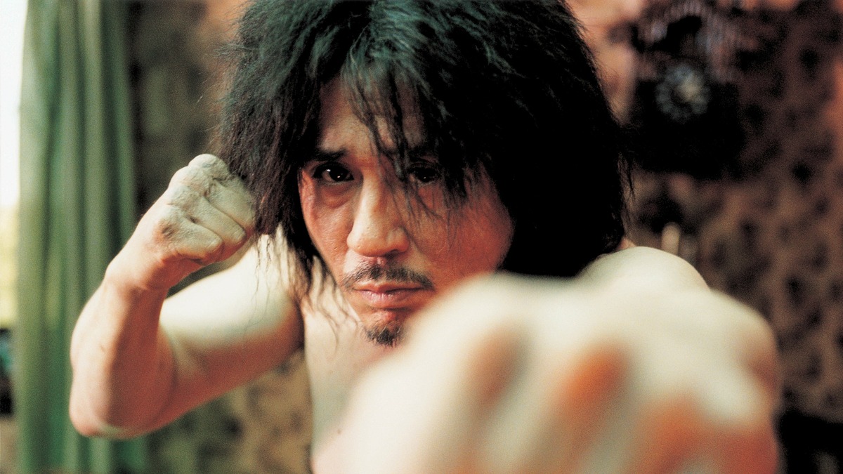 A still from 'Oldboy'. A Korean man with shaggy hair looks at the camera while standing in a martial arts pose.
