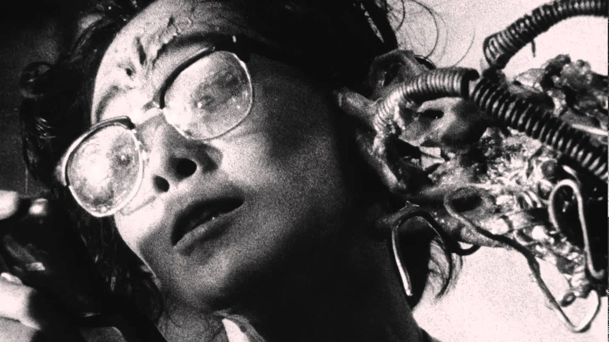 A still from 'Tetsuo: The Iron Man'. A Japanese person is shown in black and white with metal tendrils growing out of their head.