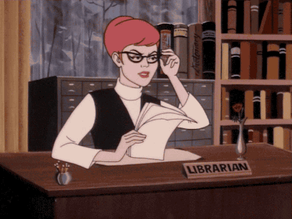 A GIF of a cartoon woman. She lowers her glasses down her face while sitting at a desk with a card that reads 'LIBRARIAN'.